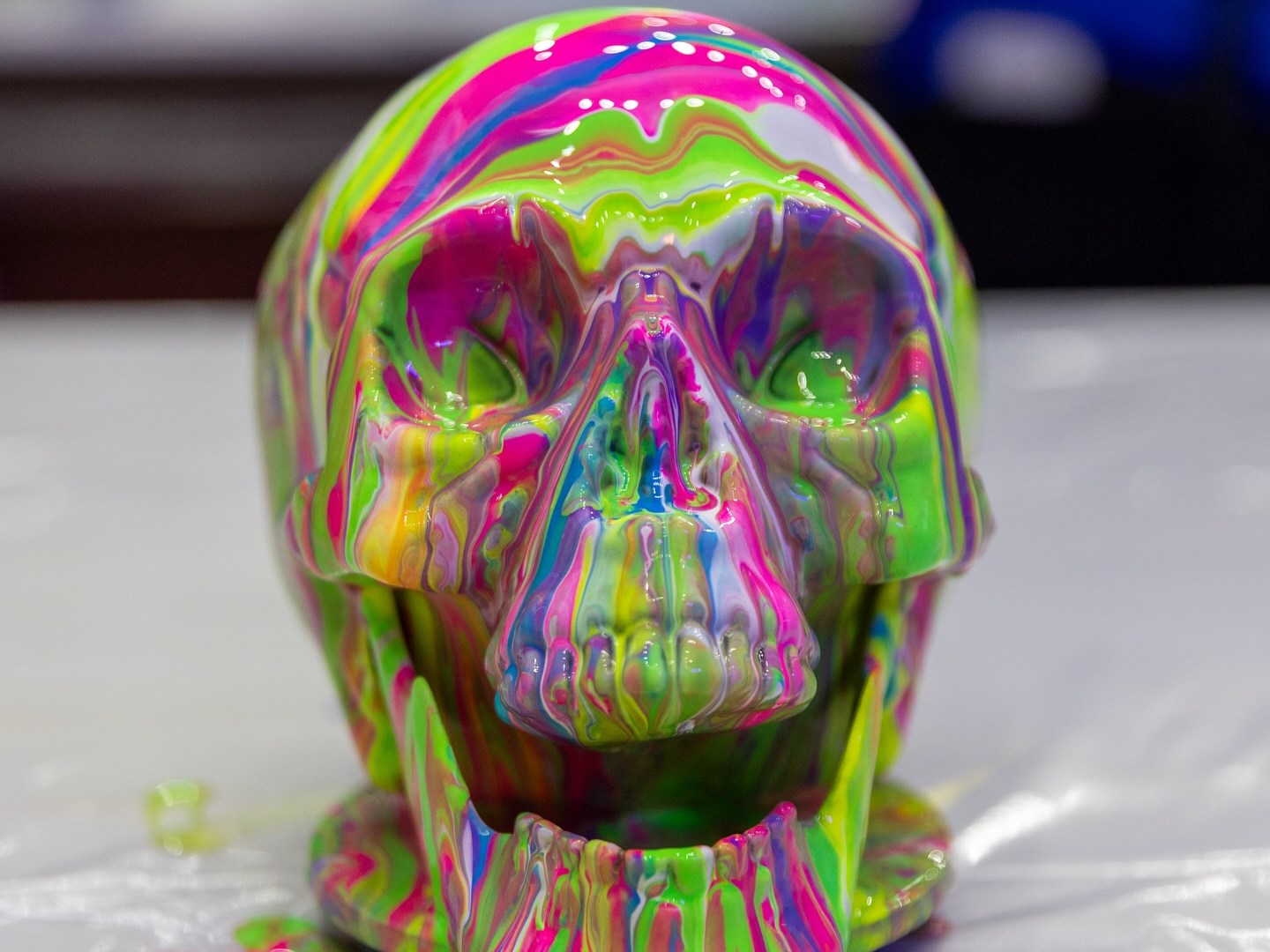 Colorful skull sculpture with dripping neon pink, green, and blue paint on table.