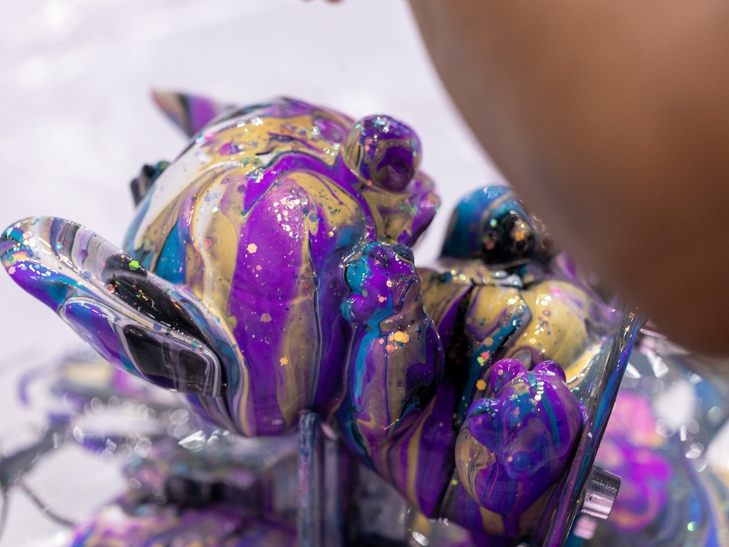 Hand painting a teddy bear sculpture with purple, gold, and blue paint.