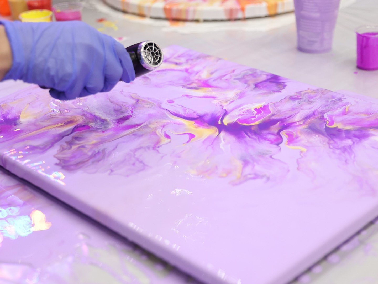 Person using heat tool on purple and orange acrylic pour painting.