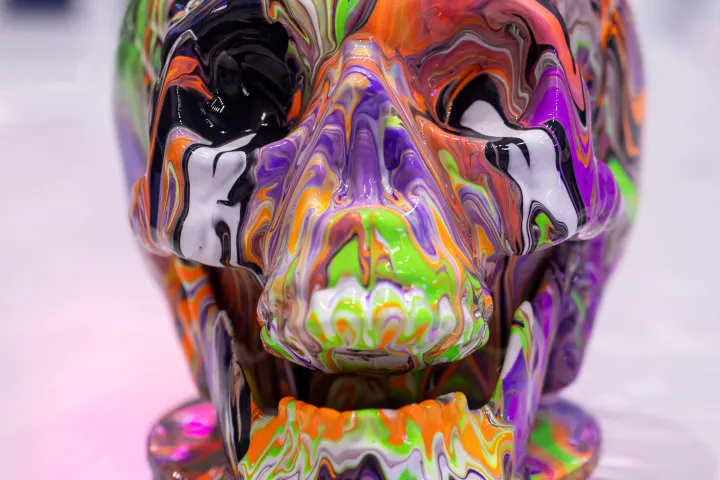 Colorful skull sculpture with swirling neon paint patterns on a white surface.