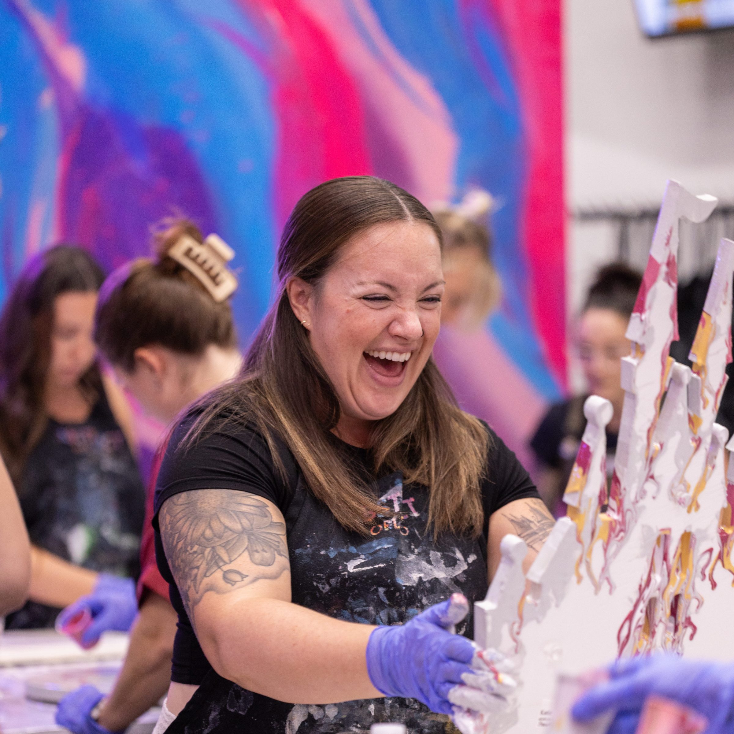 Woman laughing while painting with group on colorful background.
