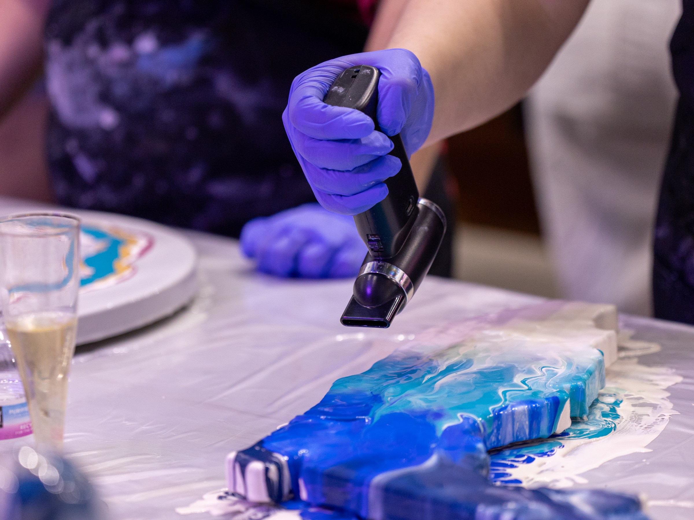 Person in gloves using heat tool on blue resin art piece.