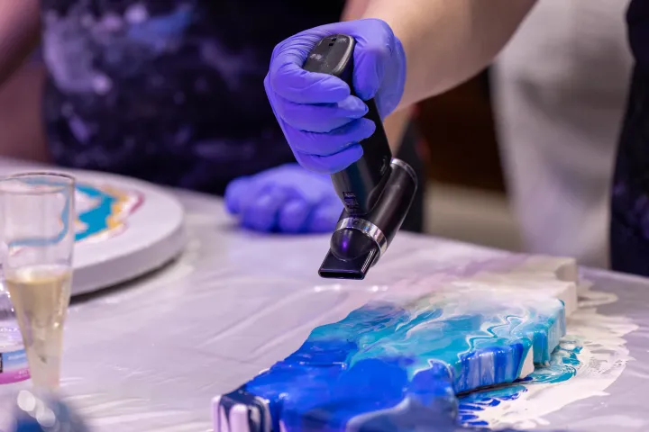 Person in gloves using heat tool on blue resin art piece.