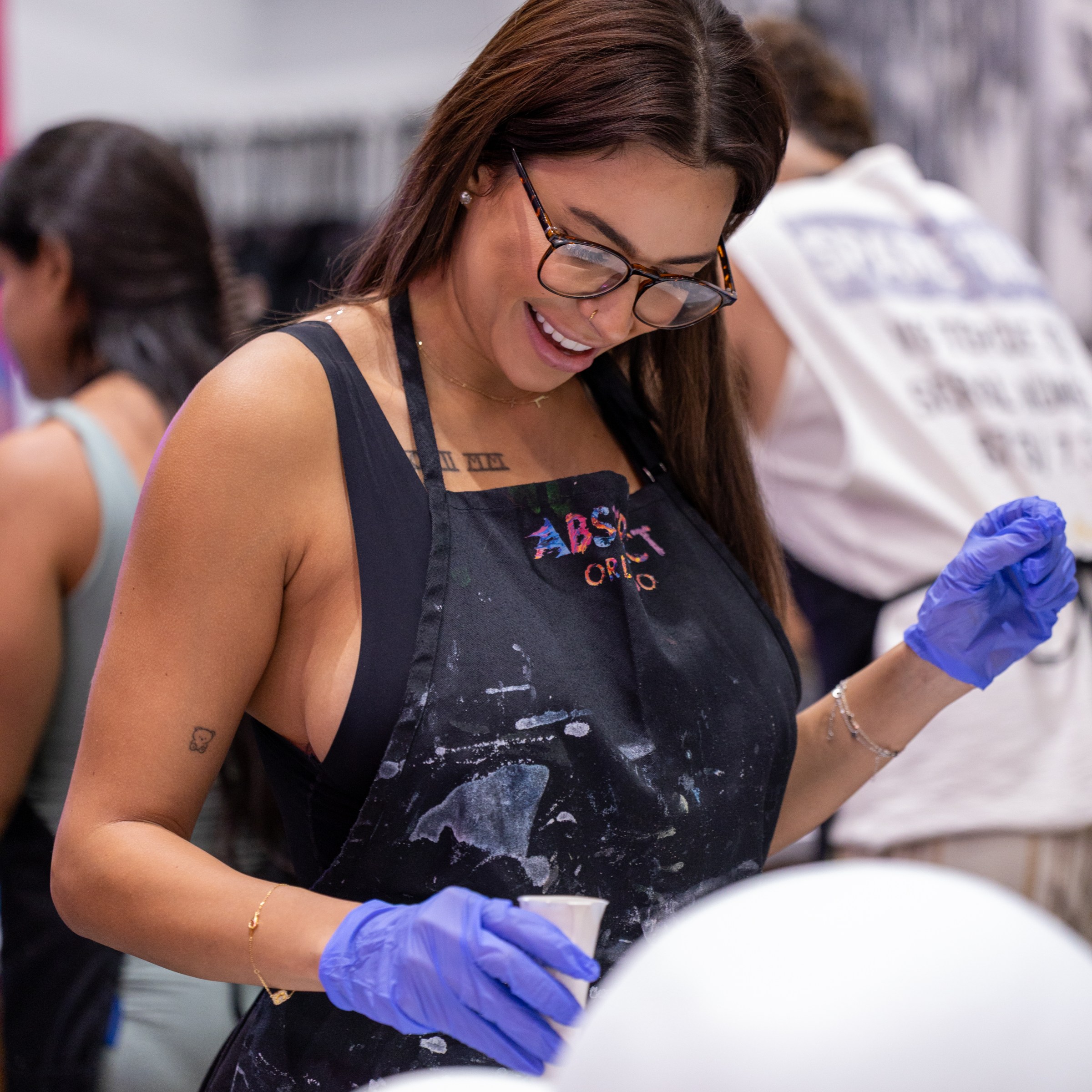 Woman in glasses and apron painting with blue gloves in an art studio.