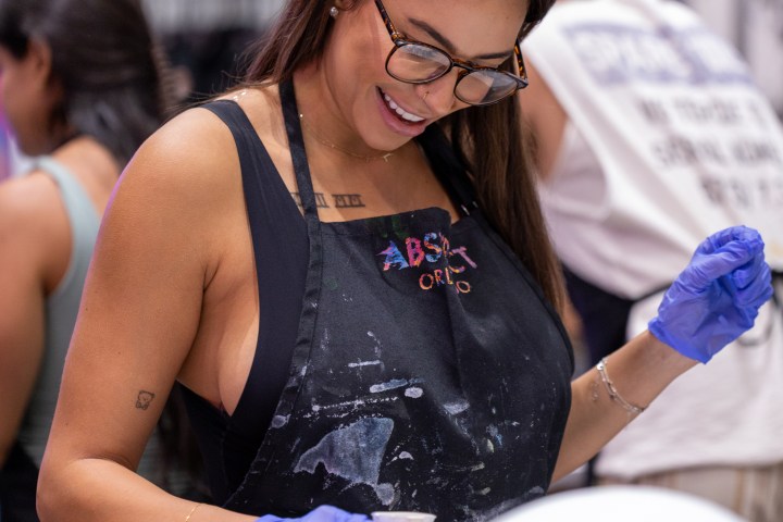 Woman in glasses and apron painting with blue gloves in an art studio.