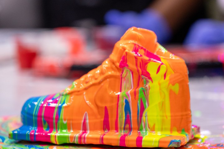 A sneaker sculpture covered in dripping neon paint on a table.