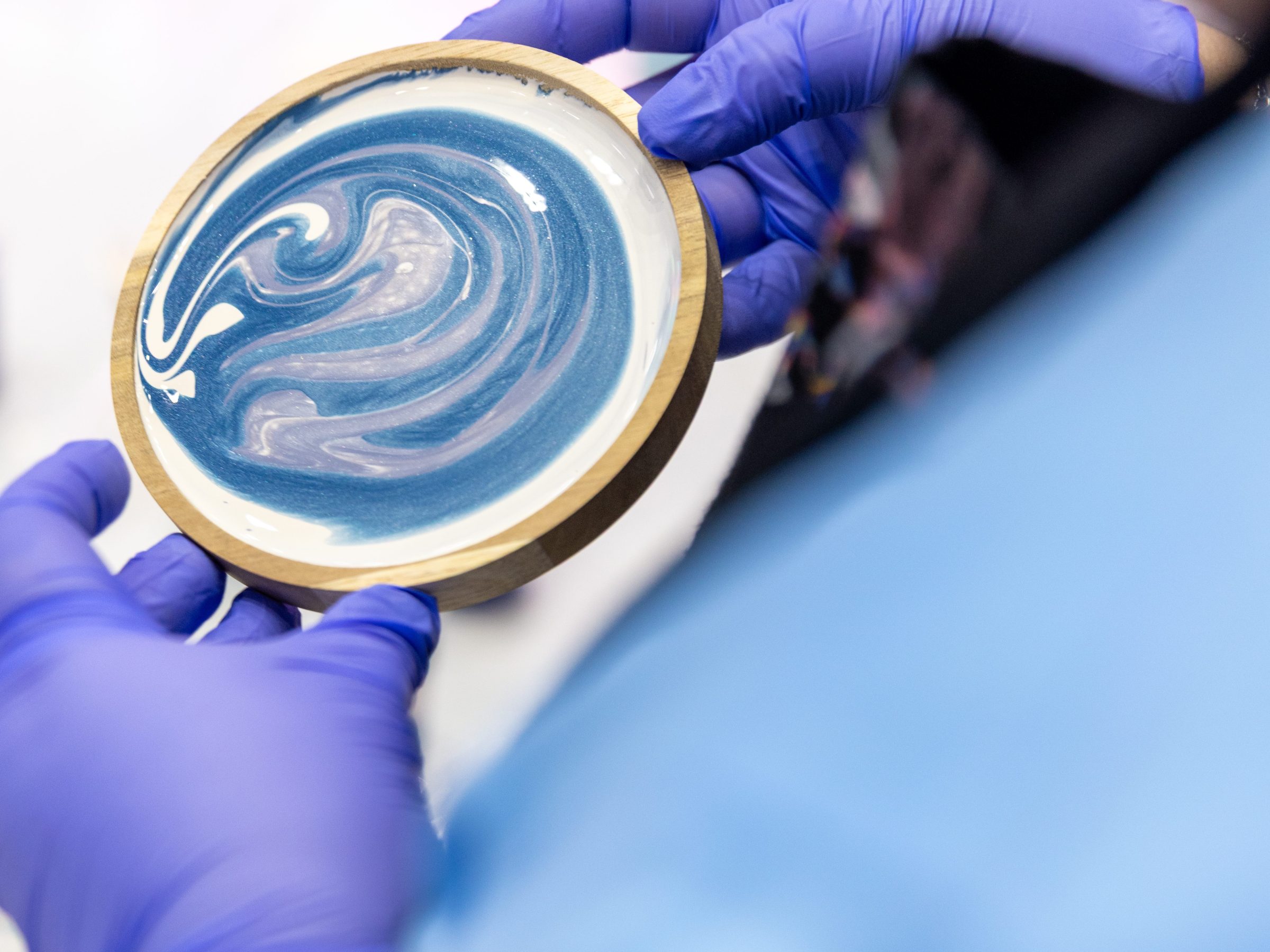 Person in blue gloves holding wood-rimmed circular object with blue and white swirl pattern.