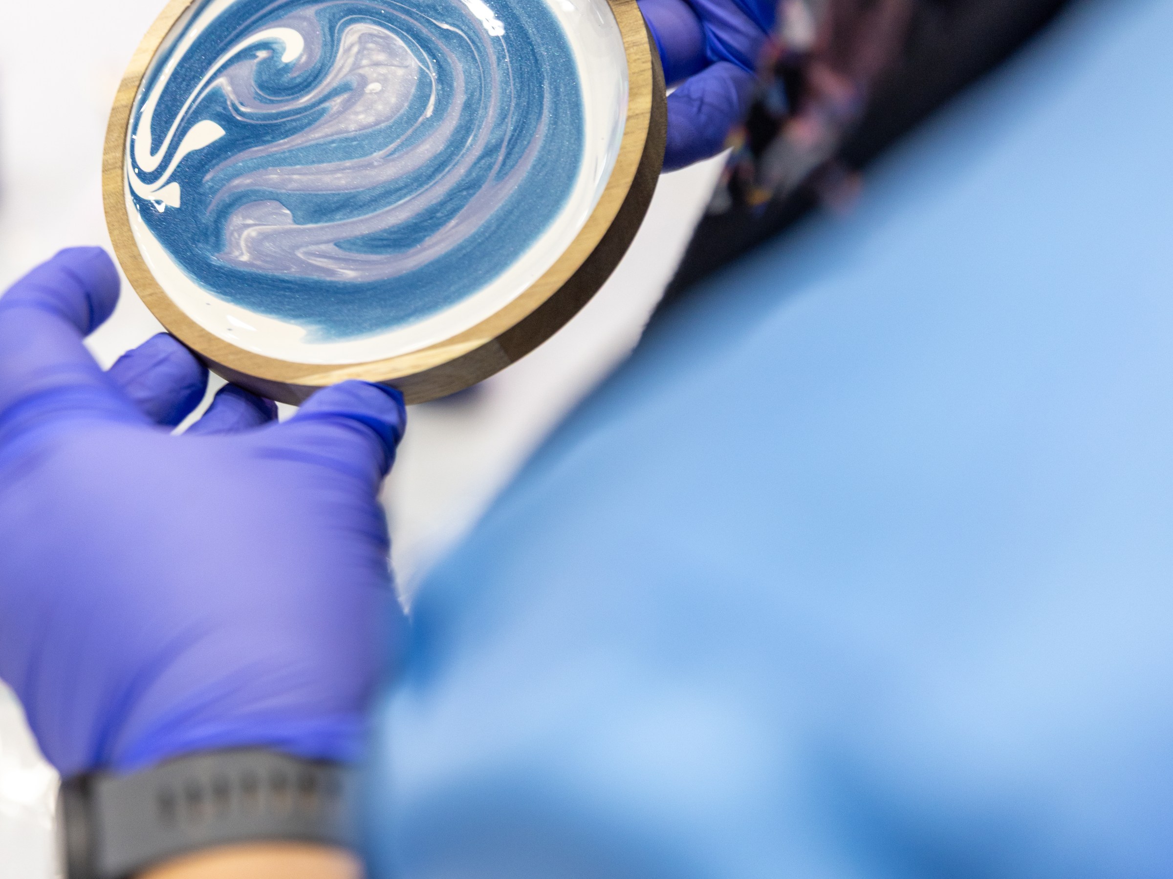 Person in blue gloves holding wood-rimmed circular object with blue and white swirl pattern.