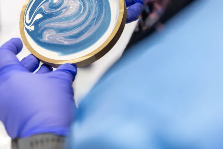 Person in blue gloves holding wood-rimmed circular object with blue and white swirl pattern.