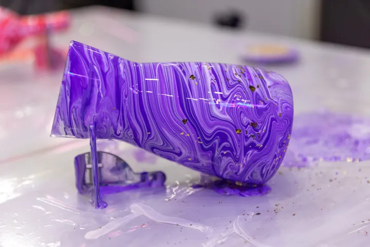 Purple marbled vase with gold flecks spills paint on a glossy surface.