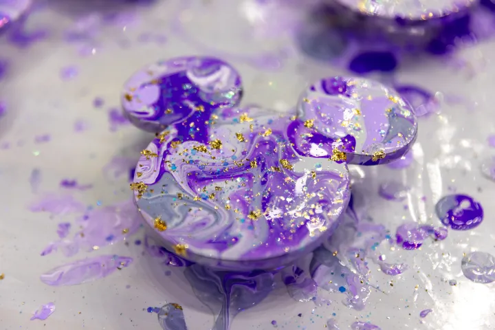 Purple and gold swirl resin in a Mickey Mouse shape on a speckled surface.