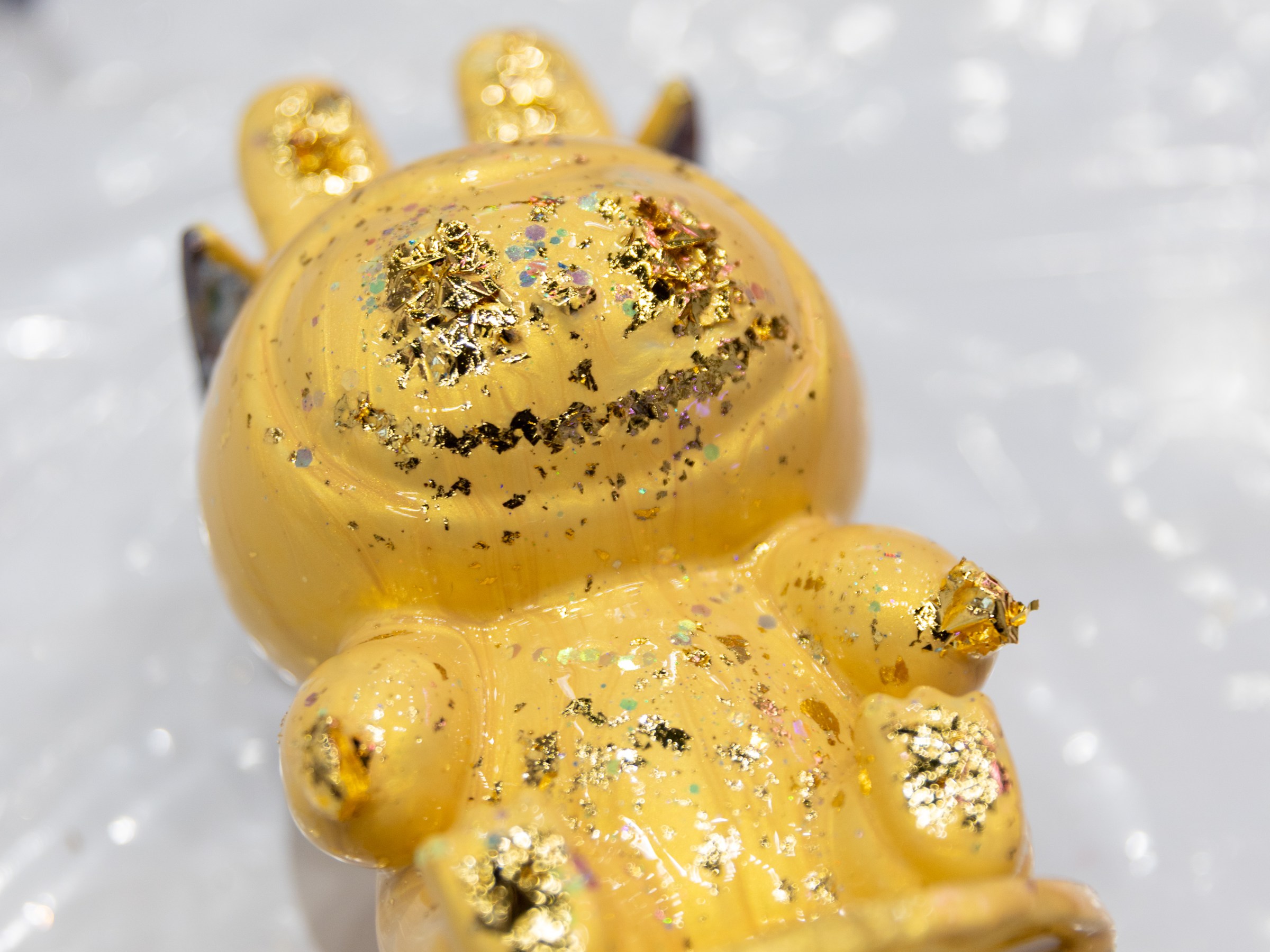 Yellow toy figurine with gold flakes on a light surface.