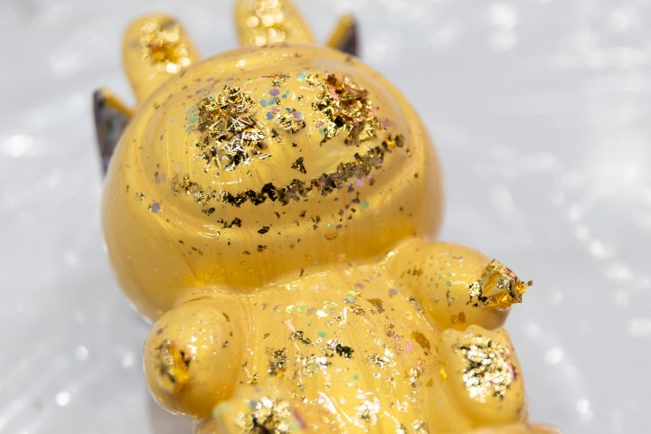 Yellow toy figurine with gold flakes on a light surface.