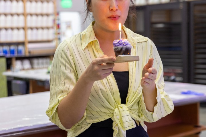Person in a striped shirt holding a cupcake with a lit candle, blurred colorful background.