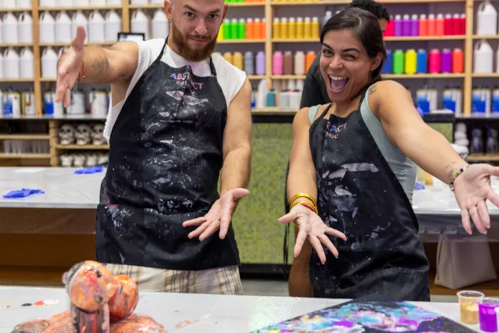 Two people in aprons posing with abstract art in a colorful paint studio.
