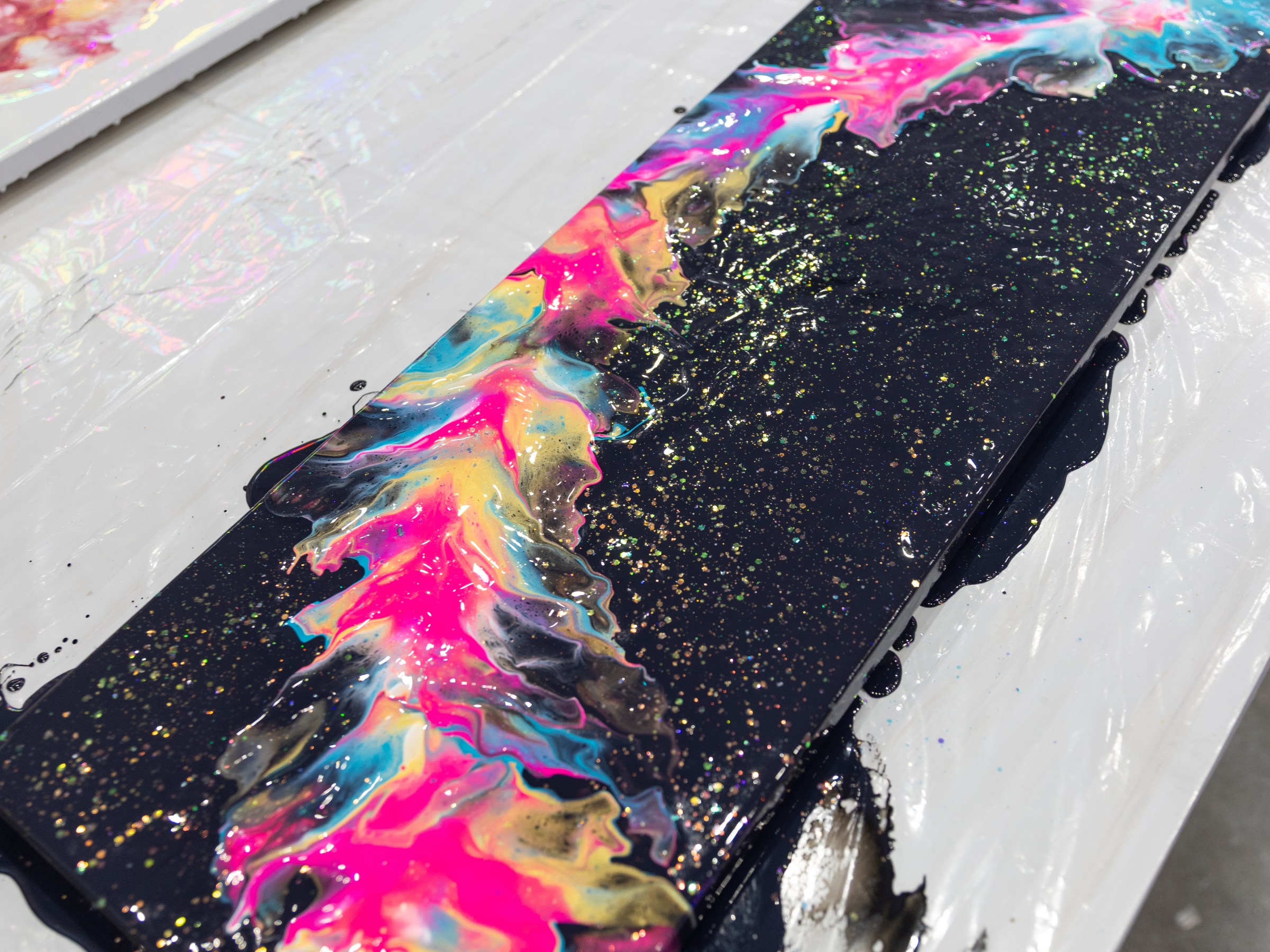 Colorful abstract painting with pink, blue, and yellow swirls on black canvas with glitter.