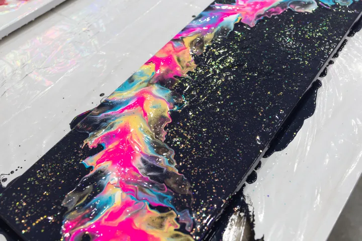 Colorful abstract painting with pink, blue, and yellow swirls on black canvas with glitter.