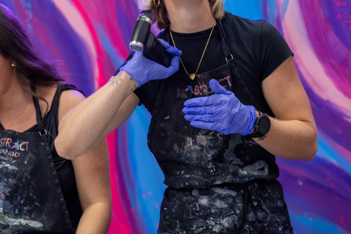 Woman in apron smiling and painting with neon sign in background.