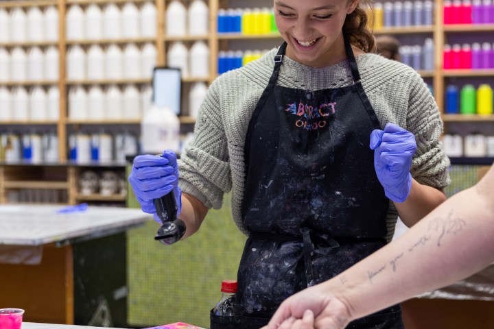 Person in apron and gloves painting with bright colors in art studio.