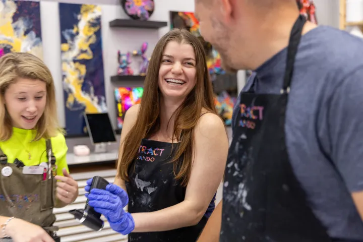 Three people in an art studio smiling, with colorful paintings on the wall.