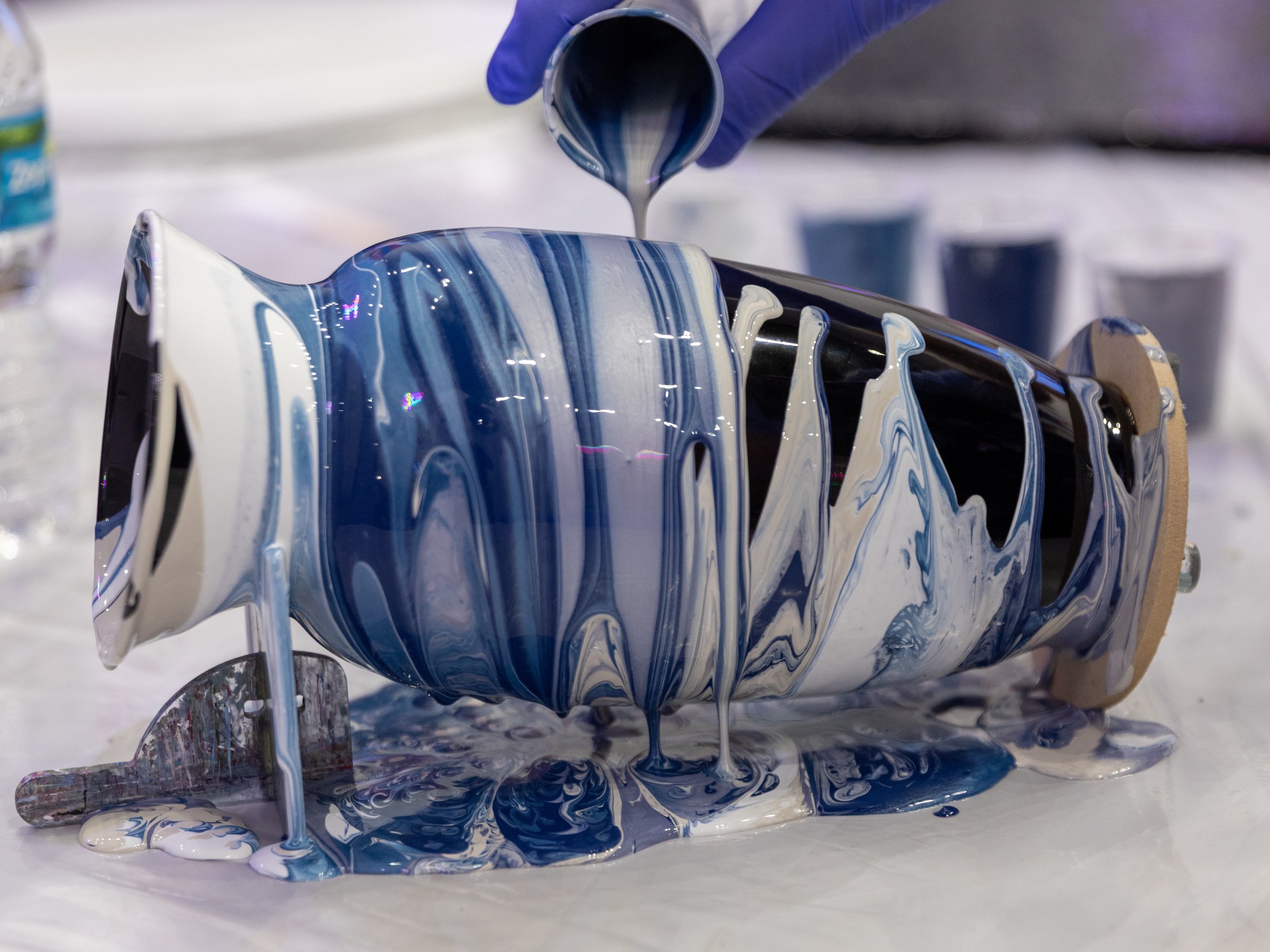 Gloved hand pours blue and white paint over a turntable for art project.