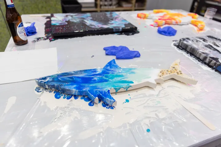 Shark-shaped resin art with blue hues on a table, surrounded by paint supplies and a bottle.