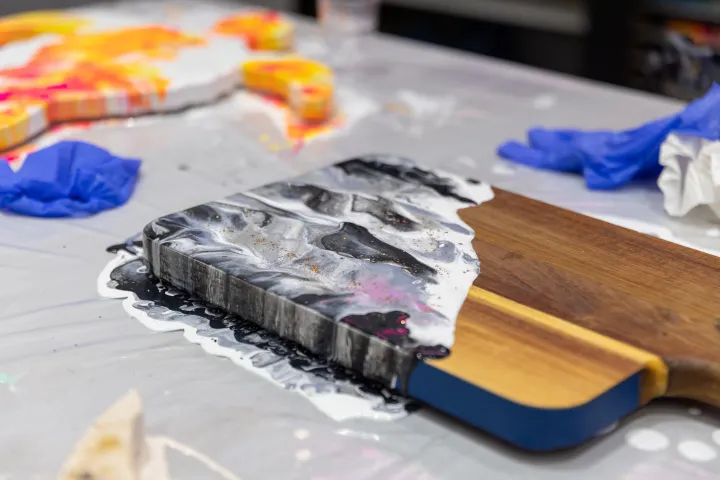 Wood board with black and white resin, blue gloves, and paper on a messy table.