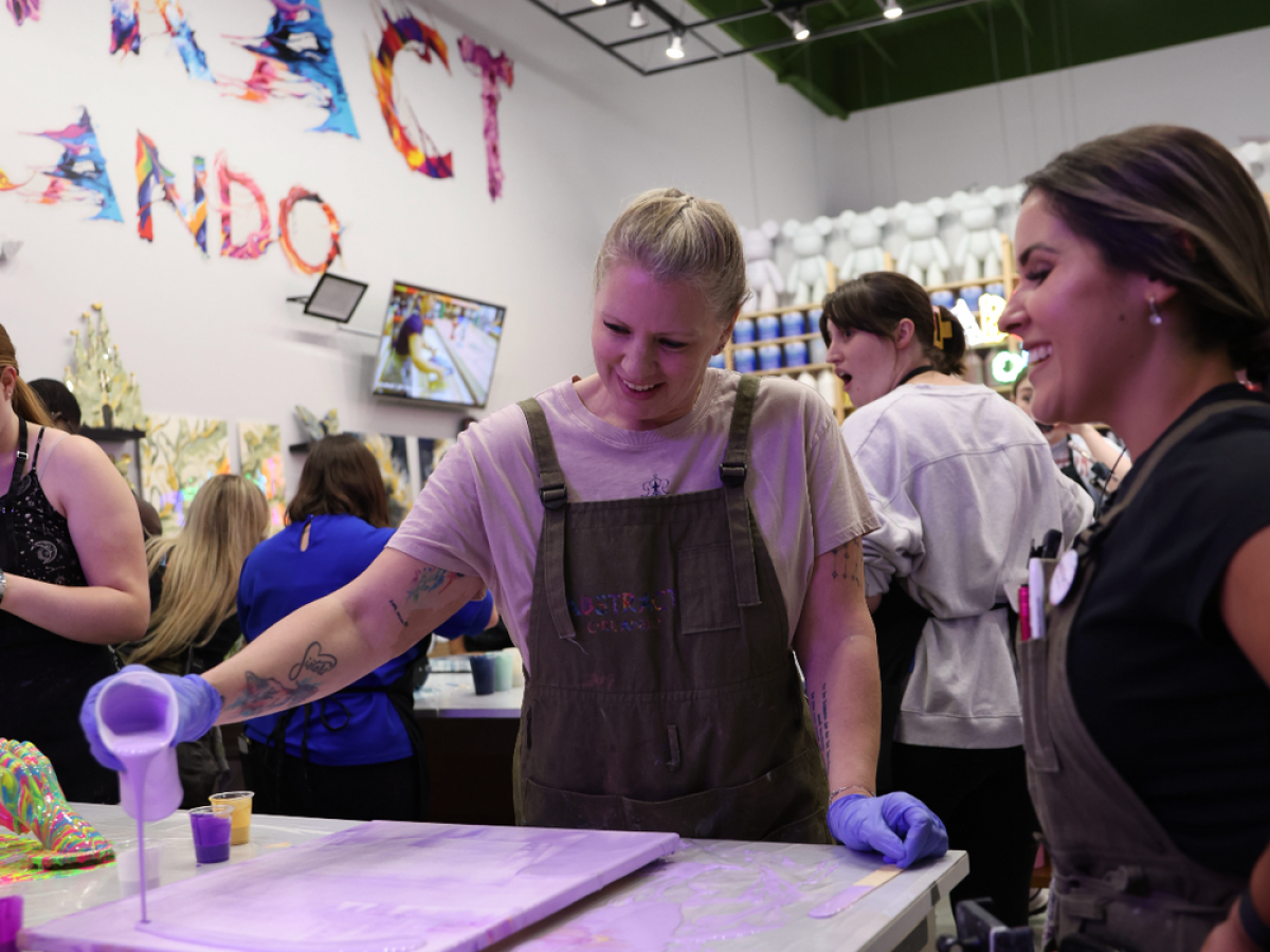 People creating art in a colorful studio, one pouring paint on a canvas.