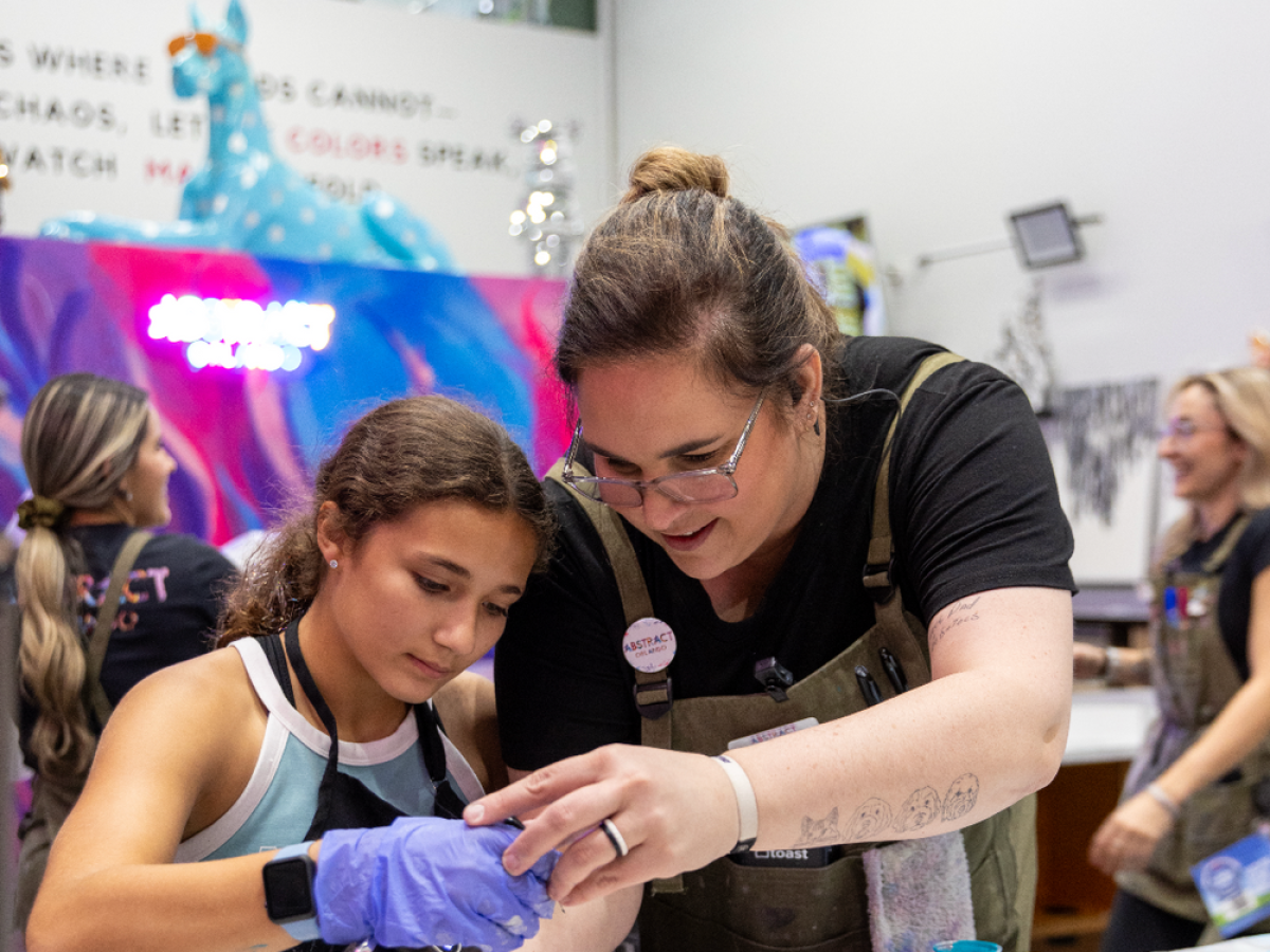 Woman and girl engaged in art activity inside colorful room with paint supplies.
