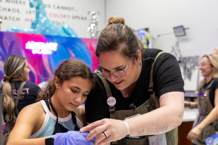 Woman and girl engaged in art activity inside colorful room with paint supplies.