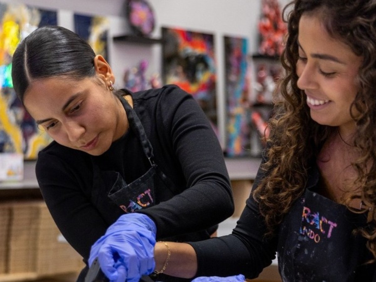 Two women in aprons and gloves creating art in a studio.