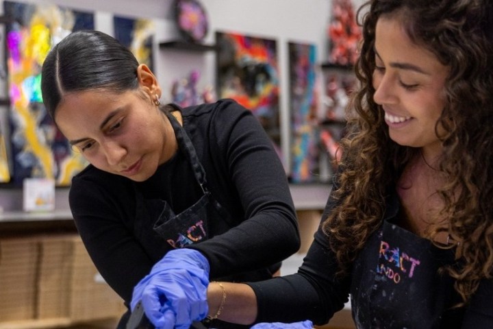 Two women in aprons and gloves creating art in a studio.