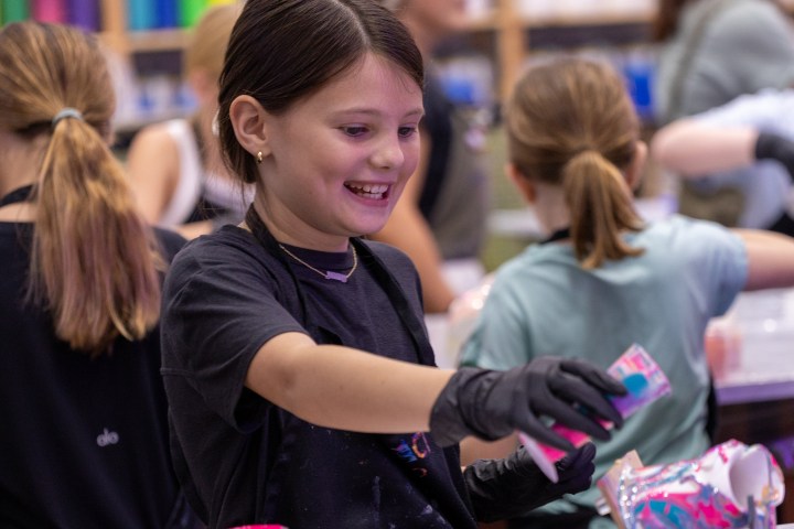 Girl in art class holding paint with colorful shelves in background.