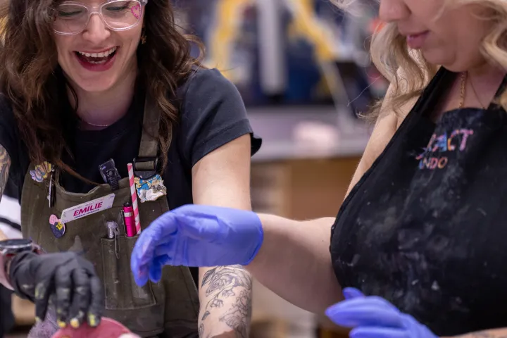 Two women joyfully painting a toy elephant with pink glaze.