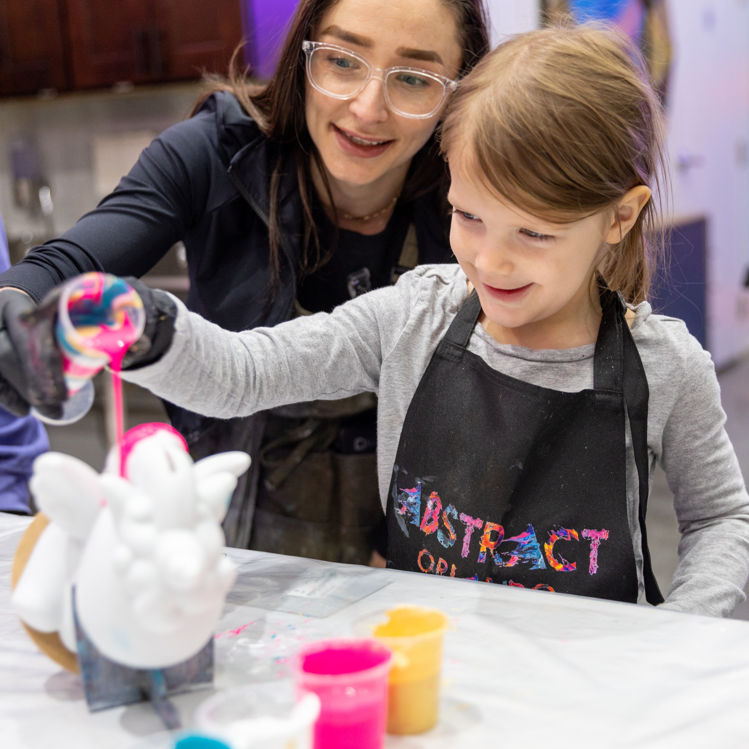 Woman and child painting ceramic unicorn together at a table.