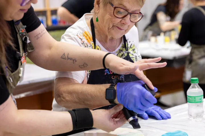 Two women painting a ceramic shape with blue and green colors in an art class.
