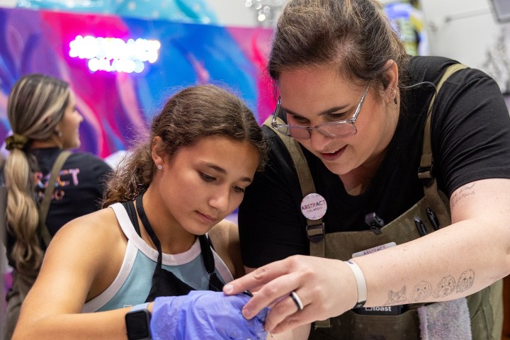 Adult assisting child in paint pouring activity at art studio.