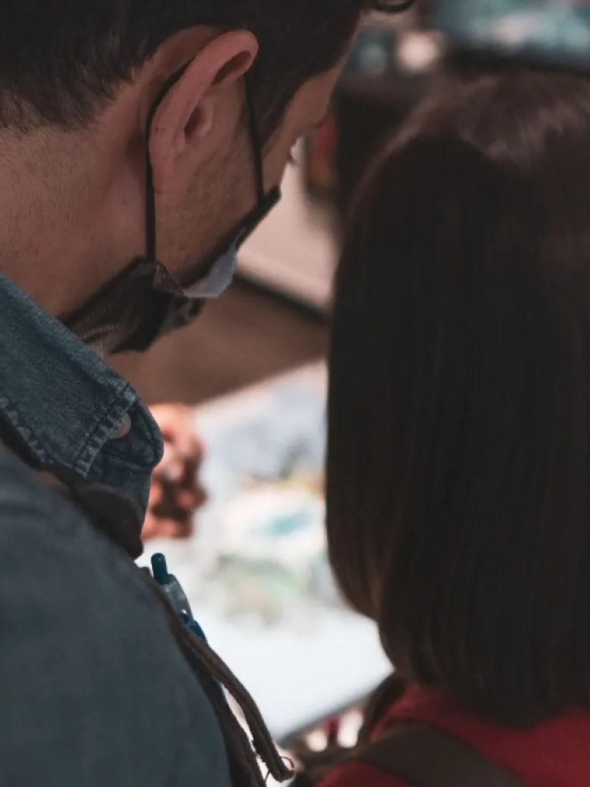 Two people from behind looking at a display; one wears a mask.