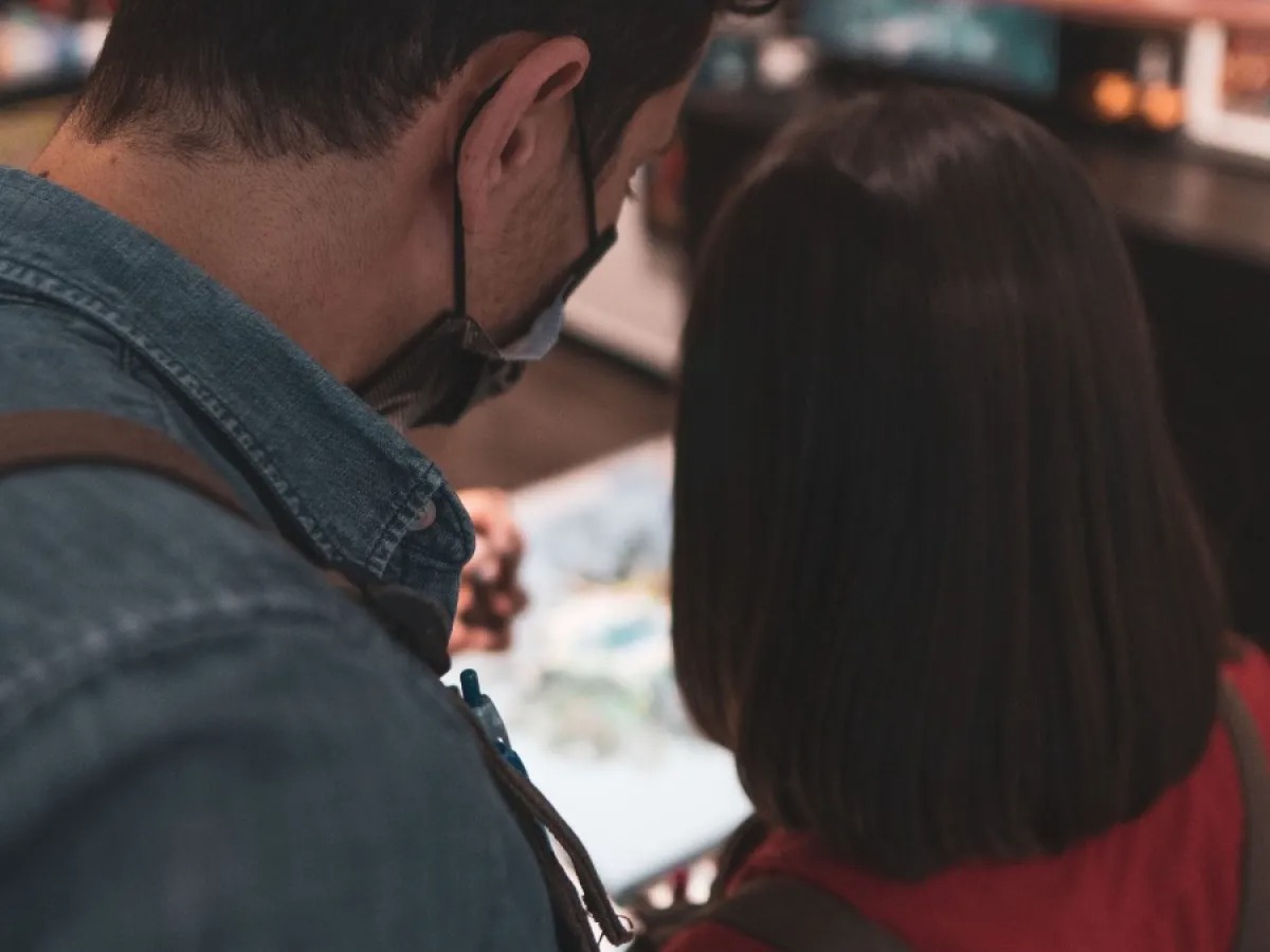 Two people from behind looking at a display; one wears a mask.