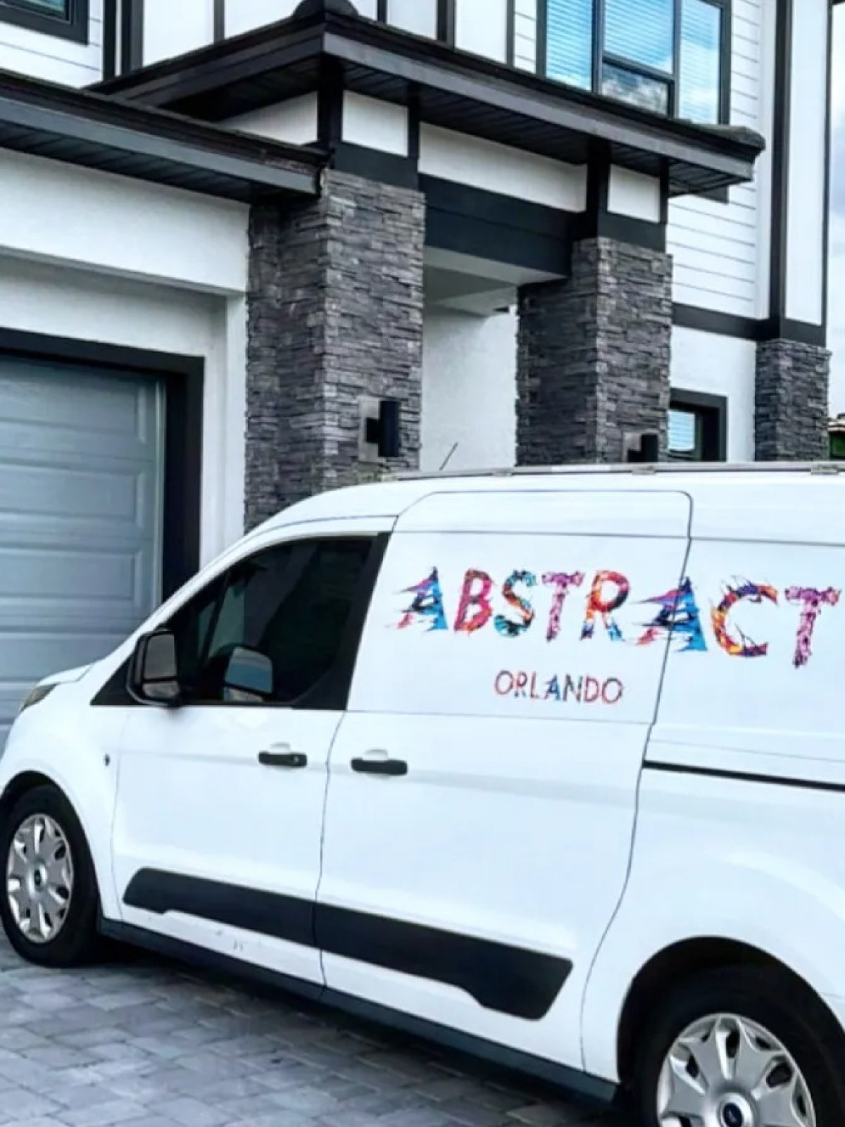 White van with colorful 'ABSTRACT ORLANDO' parked by a modern house.