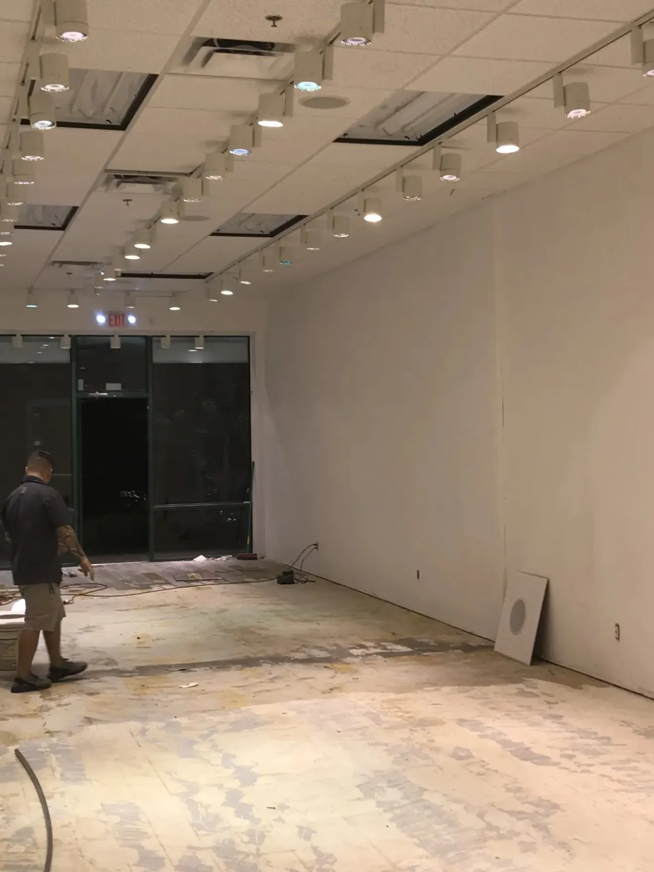 Person in an empty room with exposed flooring and overhead lights.