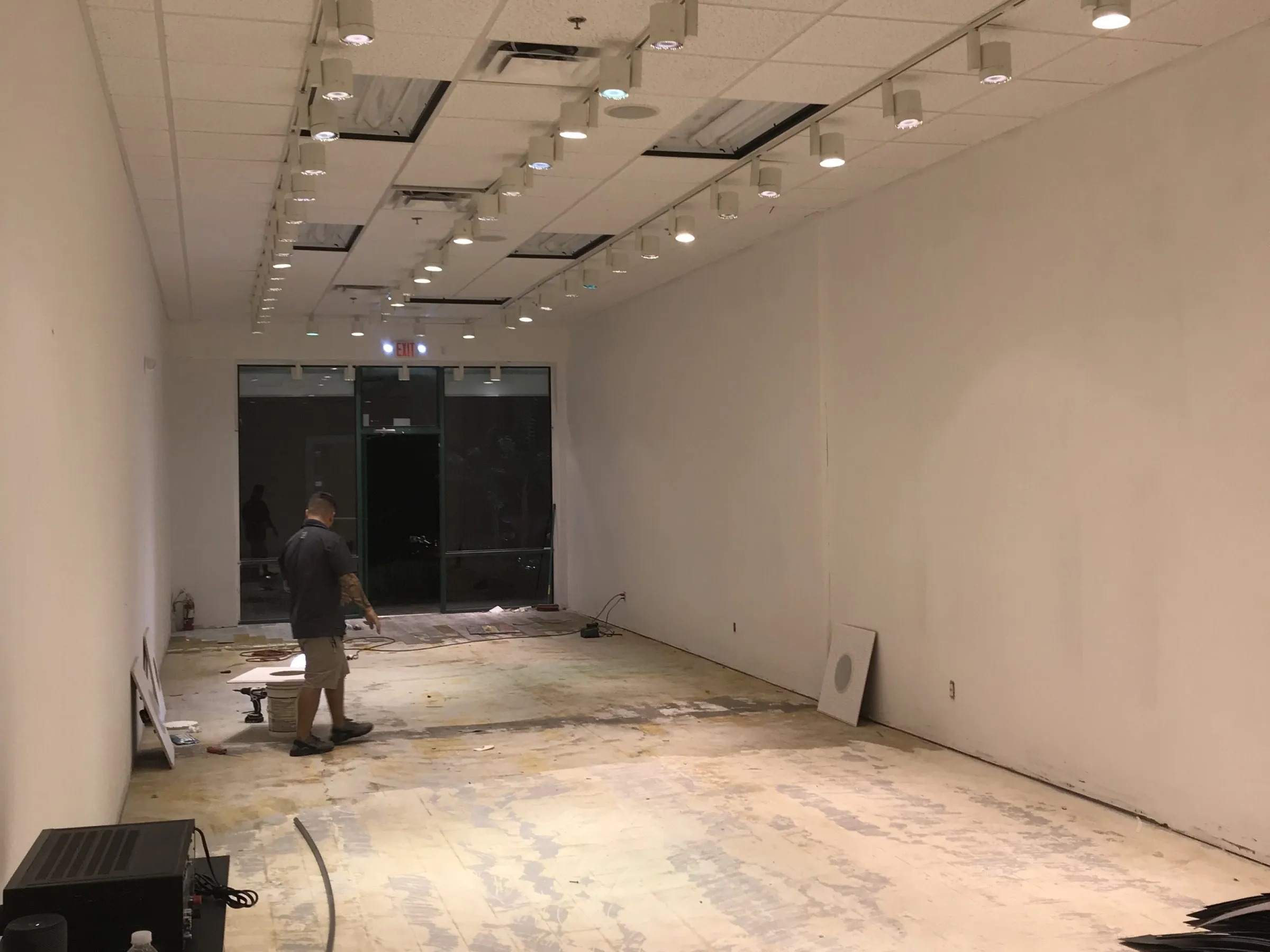 Person in an empty room with exposed flooring and overhead lights.