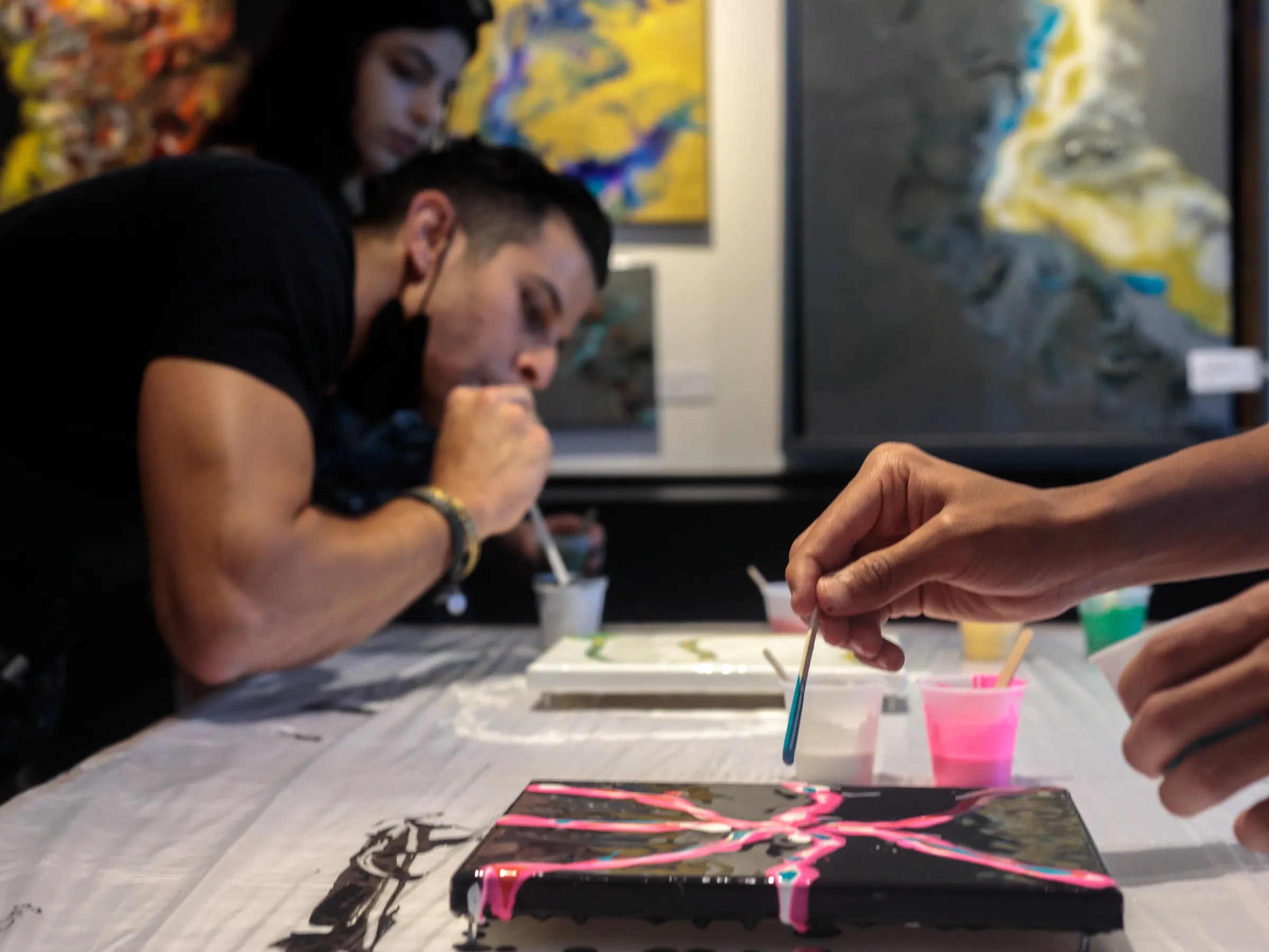 People creating abstract art with paint at a workshop table.
