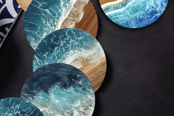Five round coasters with ocean wave designs on a dark surface, beside a patterned dish.
