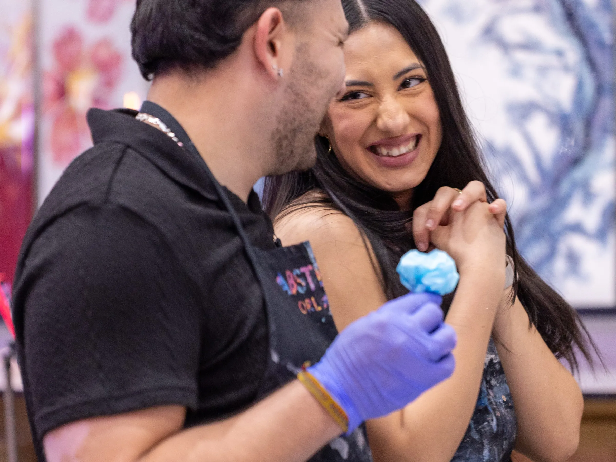 Two people smiling in an art studio, surrounded by colorful canvases.