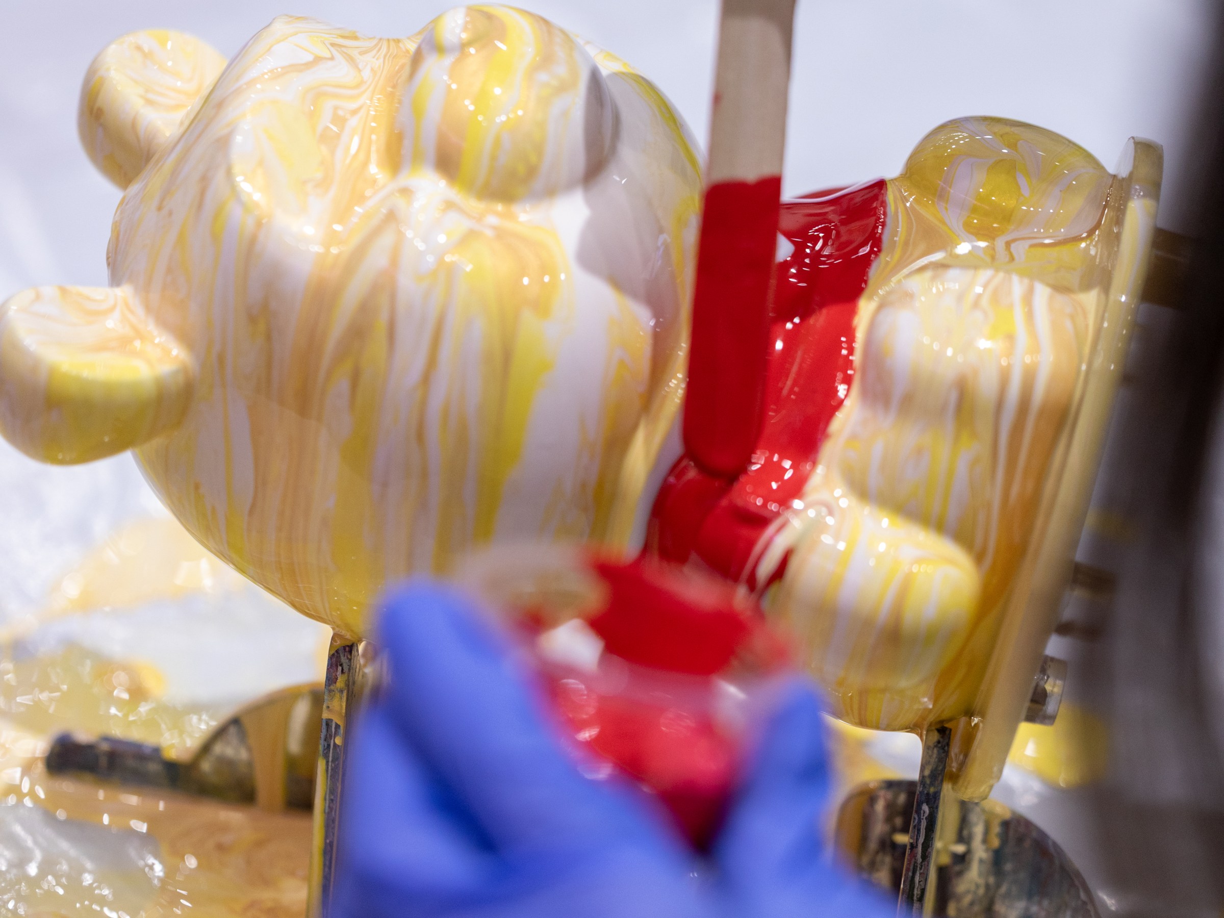 Person with gloves paints a yellow bear sculpture with red paint.
