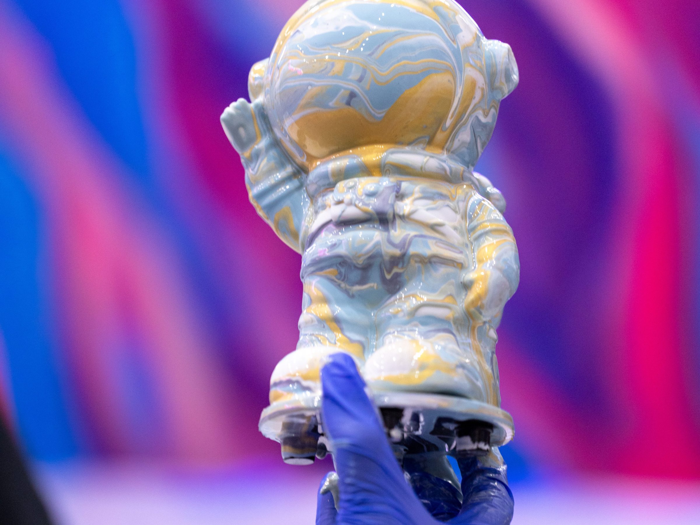 Gloved hand holding a small astronaut statue with colorful background.