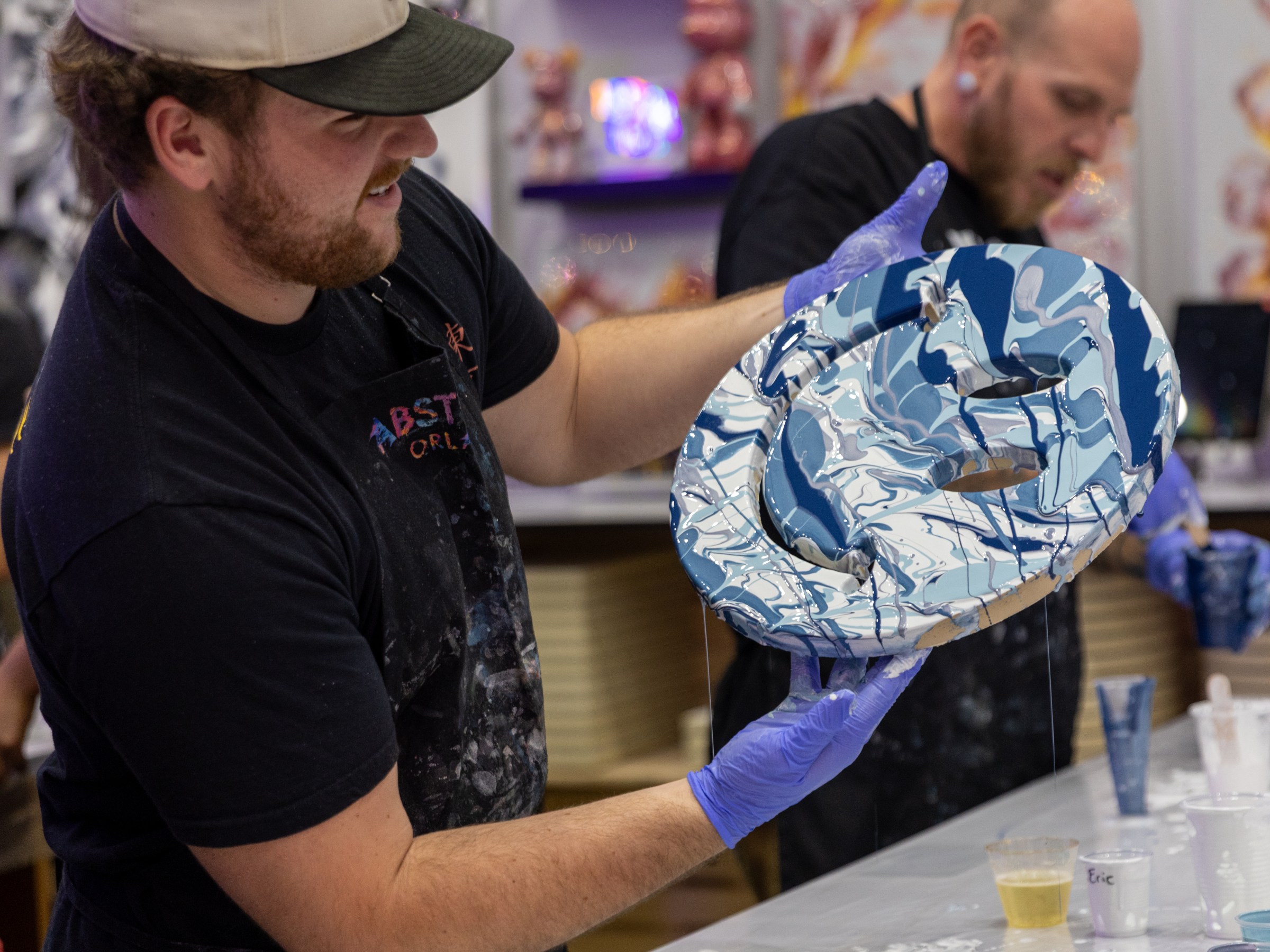 Man holding a colorful abstract resin art piece, wearing gloves and cap.