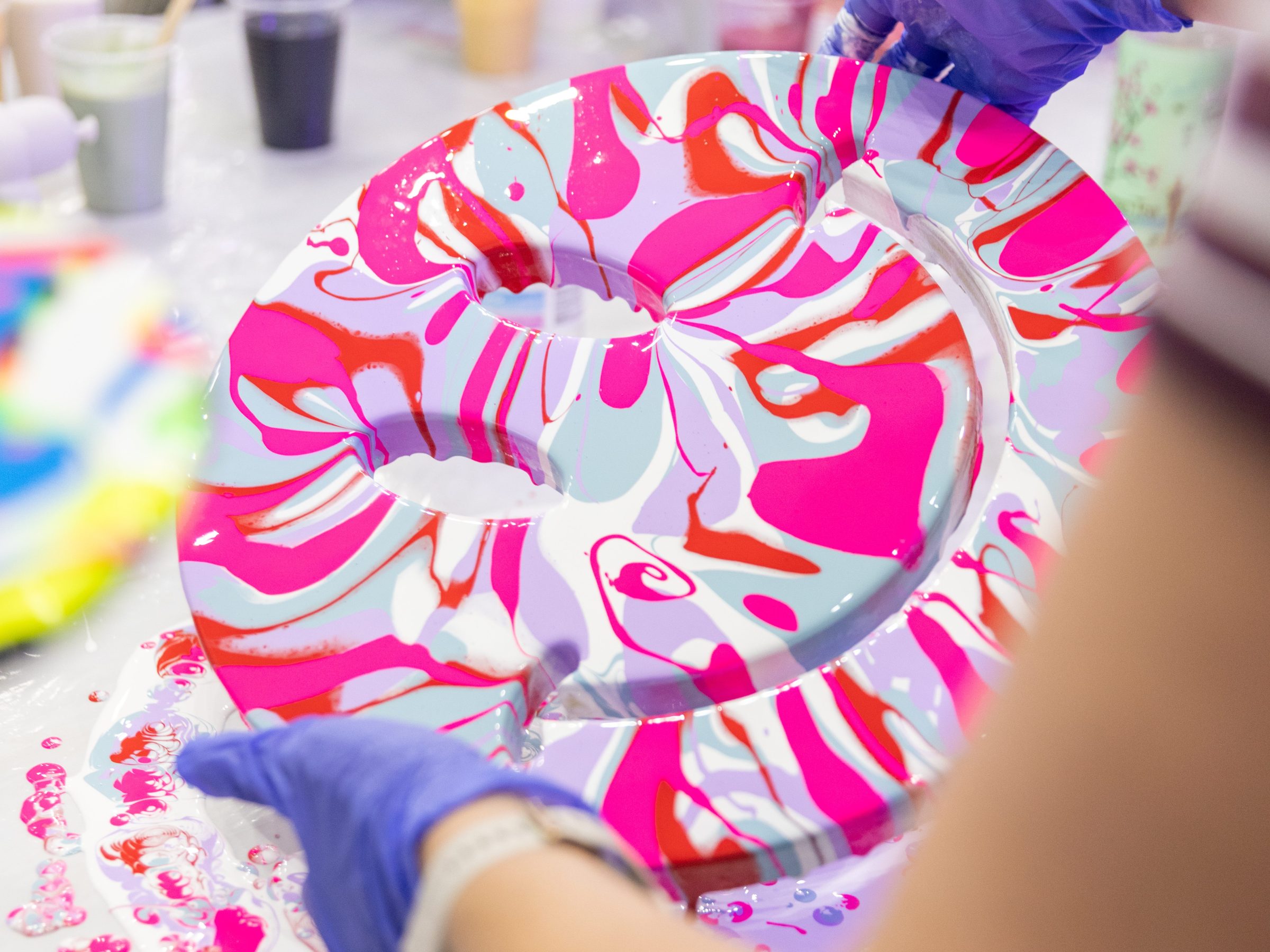 Person wearing gloves holding a colorful painted swirl art piece.