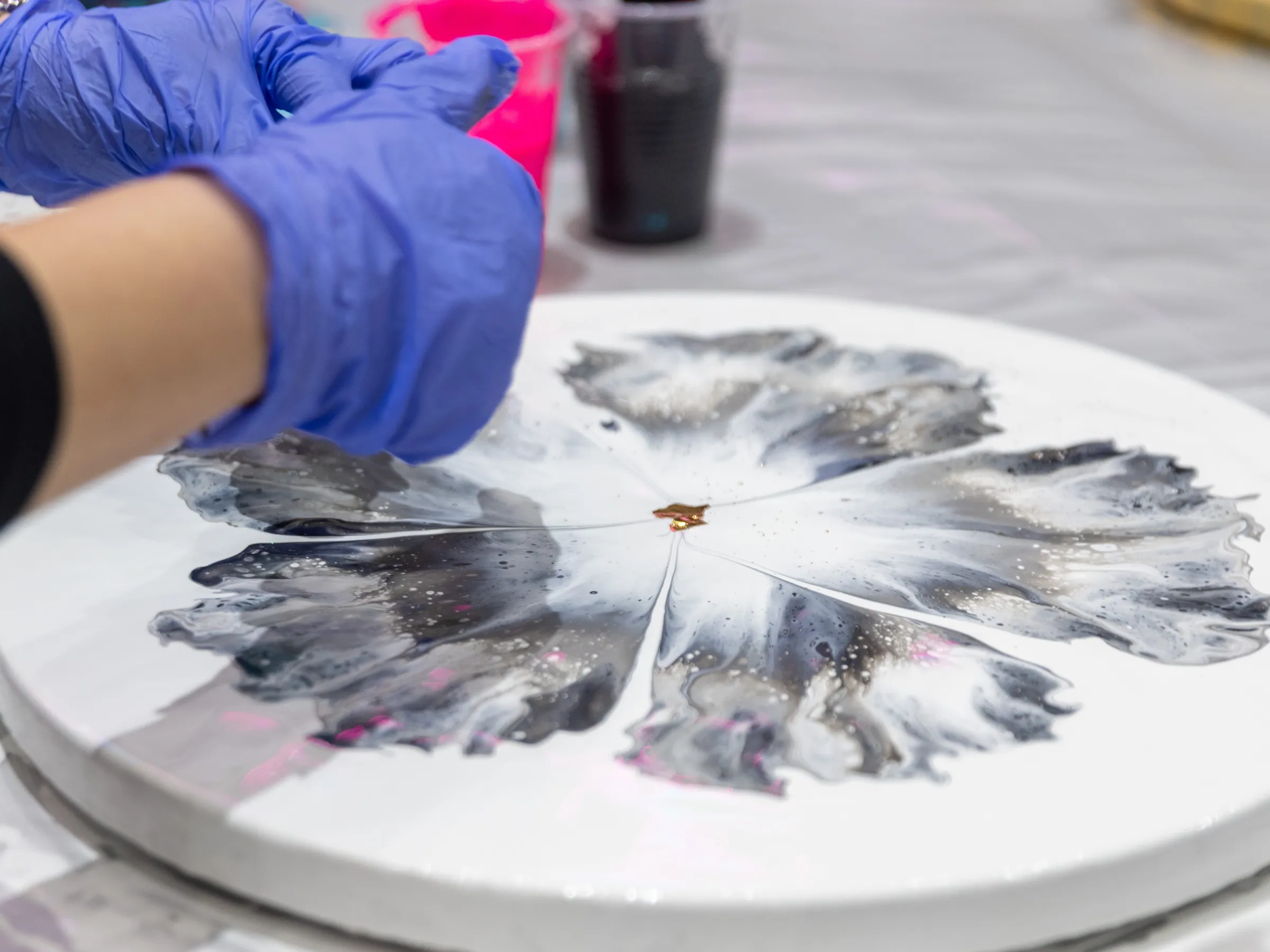 Close-up of hands in blue gloves painting abstract art on a circular canvas.